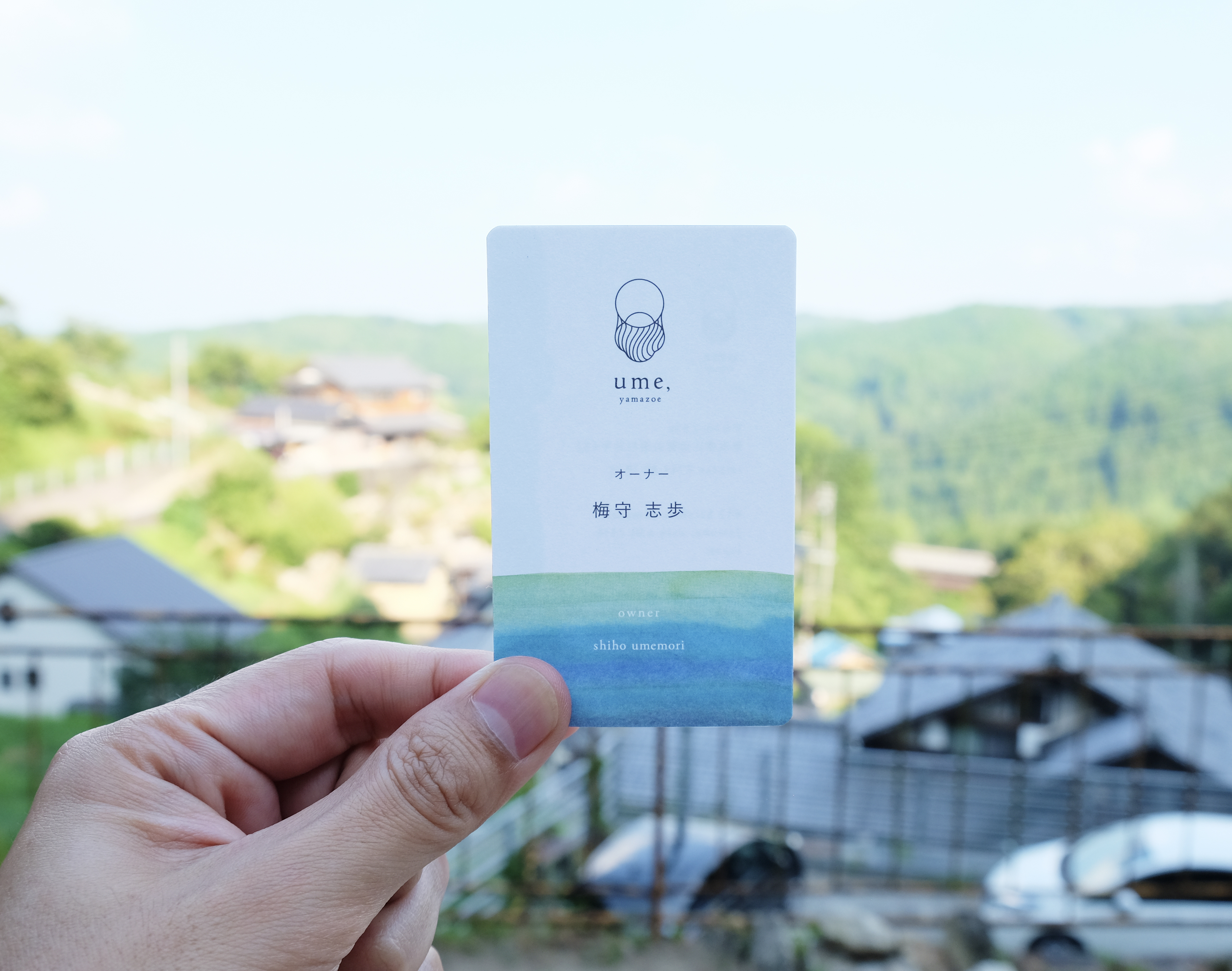 山添村の風景を背景に手に持ったume, yamazoeの名刺