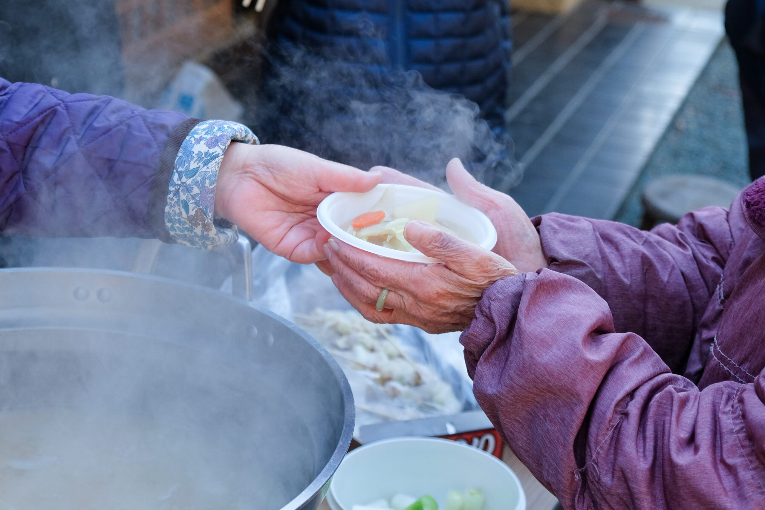 湯気の立つ鍋のそばで温かい汁物を受け渡す手元